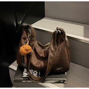 Dettaglio della borsa tote marrone scuro con ciondolo peluche su sfondo urbano moderno