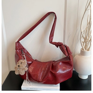 Close-up of wine red pleated dumpling bag with knot strap and plush dog charm