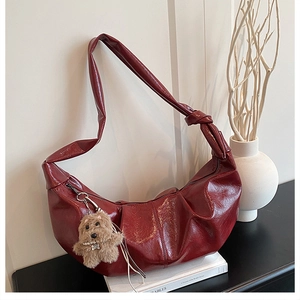 Detail of burgundy ruched hobo bag with knotted strap and cute puppy charm on books