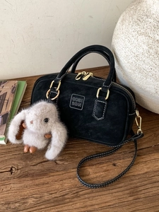 Retro black crossbody pillow bag with plush rabbit charm and gold hardware on wood surface