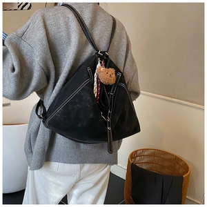 Detail of black triangular backpack with contrast stitching, bear charm, and silk scarf
