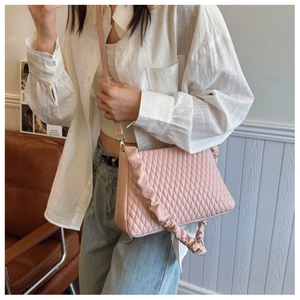 Detail of pink quilted shoulder bag featuring ruffled handle and sleek PU texture