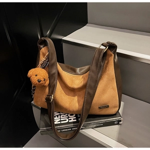 Dettaglio della borsa hobo in pelle scamosciata marrone con ciondolo a orsetto su scale grigie