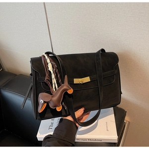 Detail of a black matte tote bag with golden twist lock and brown horse charm on a book