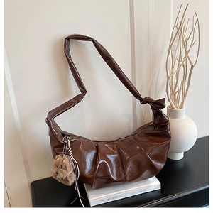 Close-up of shiny dark brown pleated crossbody bag with a cute plush puppy pendant