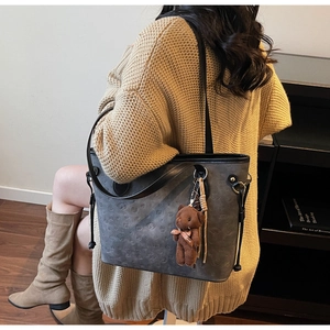 Detail of grey embossed tote bag with vintage bear patterns and plush charm on shoulder