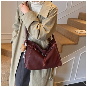 Detail view of burgundy leather hobo bag with contrast stitching and teddy bear charm