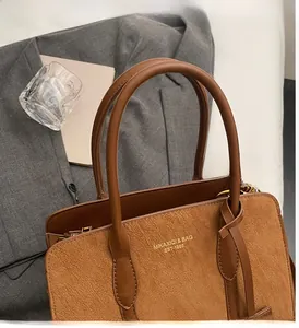 Detail der braunen Vintage-Tasche mit Wildledertextur und Logo auf grauem Blazer