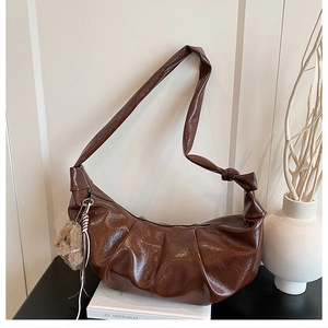 Detail of dark brown pleated crescent bag with knot strap and plush bear charm