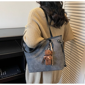 Rear view of a model wearing a grey patterned tote bag with a plush bear charm