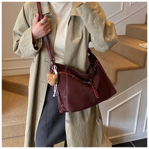 Detail of burgundy leather tote bag with white stitching and plush bear charm on a model