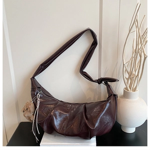 Detailed view of dark brown pleated crescent bag with cute plush bear charm on white background