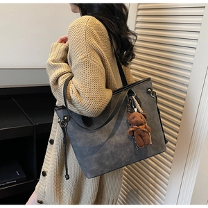 Detail of grey embossed tote bag with a cute brown bear charm and stylish shoulder strap