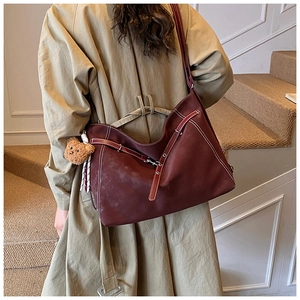 Deep red leather tote bag with white stitching and bear charm shown on model back