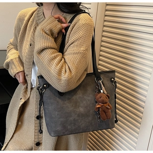 Detail of grey embossed tote bag with black strap and brown plush bear charm accessory