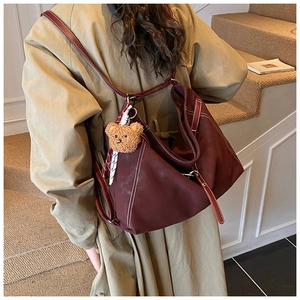 Detail of dark red tote backpack with white stitching and cute brown bear charm