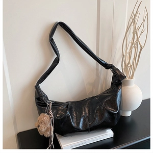 Detailed close-up of a black pleated crossbody bag with a cute brown teddy bear charm
