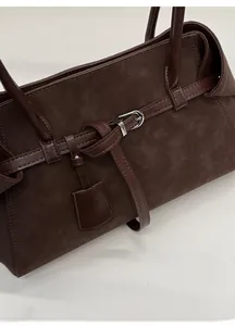 Detail of dark brown suede tote bag with leather trim, silver buckle, and decorative tag