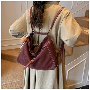 Detail of burgundy tote with contrast stitching and plush charm on casual trench coat