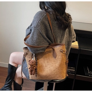 Close-up of brown tote bag featuring embossed bear patterns and a plush charm