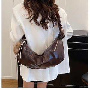 Detail of dark brown glossy croissant bag with bear pendant on white blazer