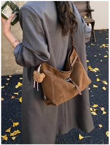 Brown suede tote bag with white stitching detail and plush bear charm outdoors