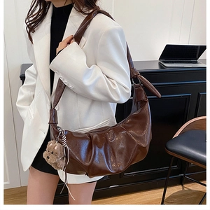 Detail of dark brown pleated crescent bag featuring glossy leather and knot strap detail