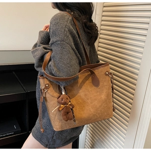 Brown suede tote bag detail featuring embossed puppy patterns and a cute plush bear charm