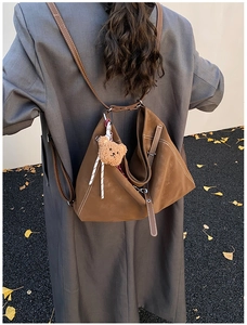 Brown suede tote bag with white stitching shown on a model in an autumn outdoor setting