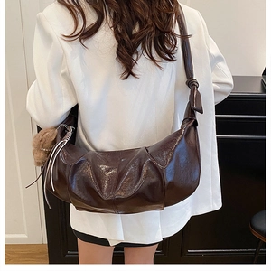 Detail of dark brown pleated crescent bag with glossy finish and plush ball charm