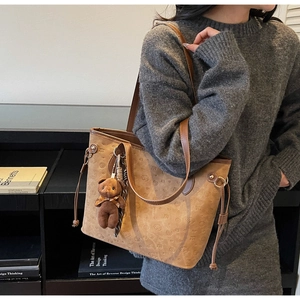 Close-up of brown embossed tote bag with a cute teddy bear charm in a lifestyle setting