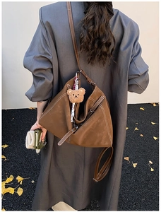 Detail of a large brown matte tote bag with a plush bear charm on a model in winter coat