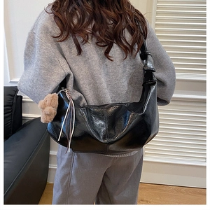 Detail of black glossy pleated crossbody bag with teddy bear charm on model shoulder