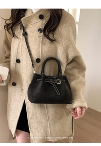 Detail of black suede bucket bag with white stitching and stylish belt buckle detail