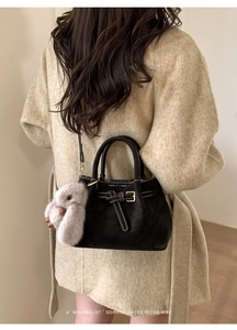Detail of black suede bucket bag with contrast stitching and plush rabbit charm