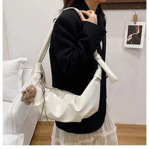 Detail of white pleated hobo bag in glossy finish with cute brown plush bear charm