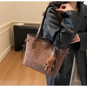 Detail of brown suede tote bag with animal head embossing and plush bear charm