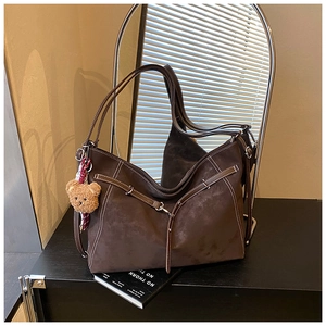 Macro detail of brown suede tote bag with white stitching and bear plush charm