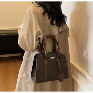 Detail der dunkelbraunen Leder-Shopper-Tasche mit Text, getragen über hellem Mantel