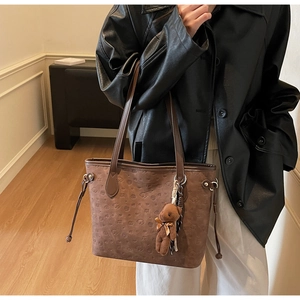 Detail view of brown textured tote bag with embossed patterns and plush bear charm