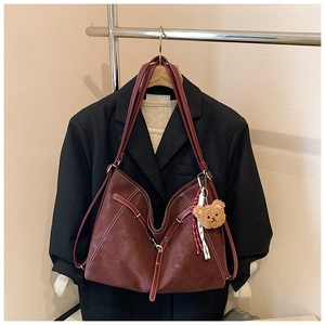 Detail of burgundy vintage tote bag with contrast stitching and teddy bear charm accessory