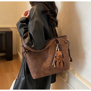 Close-up of brown tote bag with embossed puppy patterns, side studs, and plush bear charm