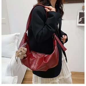 Detail view of burgundy pleated dumpling bag in shiny patent leather with bear pendant