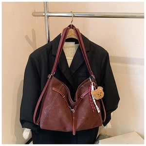 Detail of red-brown vintage tote bag with contrast stitching and plush bear charm