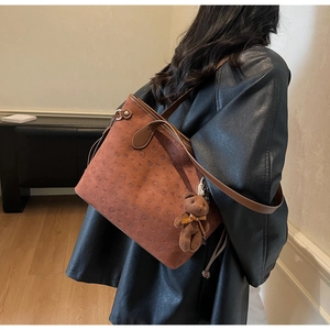 Close-up of brown suede tote bag with embossed bear patterns and plush bear charm decoration