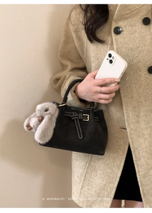 Detail of black suede tote with white contrast stitching and a plush rabbit pendant