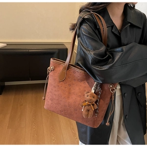 Detailed shot of brown tote bag with embossed puppy patterns and a cute teddy bear charm