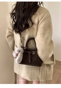 Detail of dark brown suede bucket bag with white contrast stitching and plush bunny charm