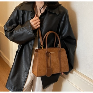 Nahaufnahme der braunen Wildleder-Handtasche mit goldener Logo-Prägung und Schultergurt