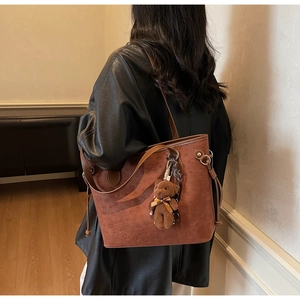 Detail of a brown leather tote bag with cartoon patterns and a teddy bear plush charm